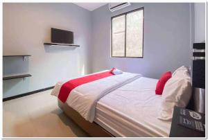 RedDoorz Syariah near T2 Juanda Airport 2 في Dares: غرفة نوم بسرير ومخدات حمراء ونافذة
