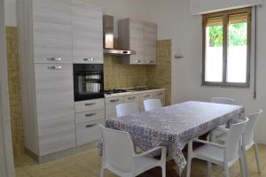 uma cozinha com uma mesa com cadeiras brancas e uma cozinha com um fogão em Cala Rosa em Torre Lapillo