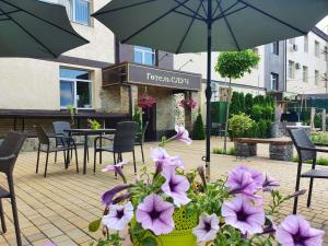 a patio with purple flowers and chairs and an umbrella at Hotel Sluch in Starokostyantyniv