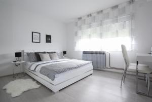 a white bedroom with a bed and a desk and a window at Imperium Rooms Zagreb Airport in Velika Gorica