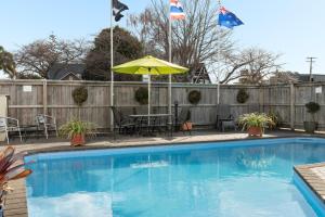 - Piscina con mesa, sombrilla y banderas en ASURE Macy's Motor Inn, en Tauranga