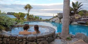 two people sitting in a pool in a rock wall at Belle Glamping by the Sea in Katikati