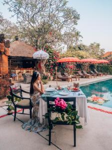 une femme assise à une table à côté d'une piscine dans l'établissement The Pavilions Bali, à anur