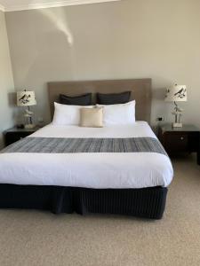 1 dormitorio con 1 cama grande, 2 mesas y 2 lámparas en Federation Motel Resort - Corowa, en Corowa