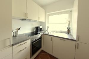 eine Küche mit weißen Schränken, einem Waschbecken und einem Fenster in der Unterkunft Nordseesonne I in Wenningstedt-Braderup