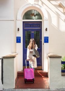 Uma mulher a tirar uma mala cor-de-rosa de uma porta azul. em Dolphin Inn - The Lodge em Londres