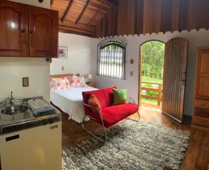 a kitchen with a bed and a red chair in a room at Chalés Lua de Mel in Monte Verde