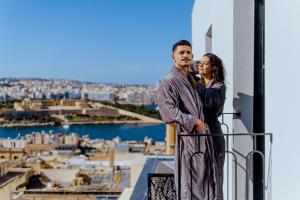 a man and a woman standing on a balcony looking at the city at The Embassy Valletta Hotel in Valletta