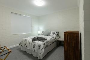 a white bedroom with a bed and a window at Apparition Apartments in Geraldton