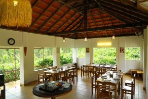 un restaurante con mesas y sillas de madera y ventanas en Dhanagiri Home Stay en Vythiri