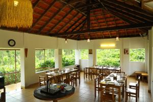 un restaurante con mesas y sillas de madera y ventanas en Dhanagiri Home Stay, en Vythiri