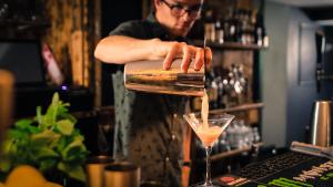 ein Barkeeper, der einen Drink in einem Cocktailglas macht in der Unterkunft Hideout Hostel in Morzine