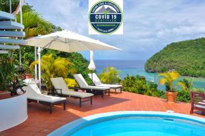 a pool with chairs and an umbrella and the ocean at Marigot Palms Luxury Caribbean Apartment Suites in Marigot Bay