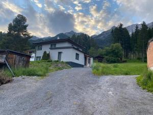 une maison blanche sur une route en gravier avec des montagnes en arrière-plan dans l'établissement Appartement Klein Tirol, à Pettneu am Arlberg
