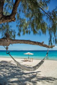 a hammock on a beach with an umbrella and the ocean at Constance Tsarabanjina - All Inclusive in Nosy Mitsio