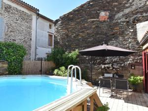 a swimming pool with an umbrella next to a building at Holiday home with pool in Cuxac Cabard s in Cuxac-Cabardès