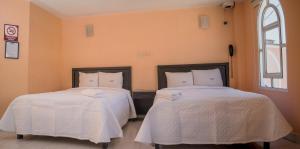 two beds with white sheets in a room with a window at Hotel Express Alejandría in Xalapa