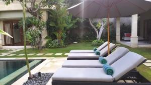 four lounge chairs with an umbrella next to a pool at Villa Zanissa in Seminyak