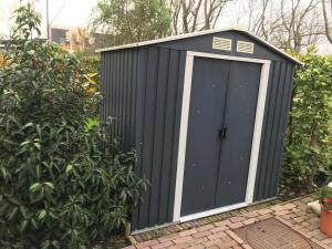 a black shed with a door in a garden at Houseboat Linquenda in Woubrugge