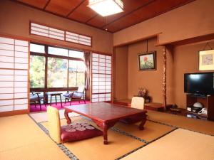 a living room with a table and a tv at Maruka Ryokan in Yamanouchi