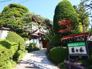 a sign in front of a house with bushes at Maruka Ryokan in Yamanouchi