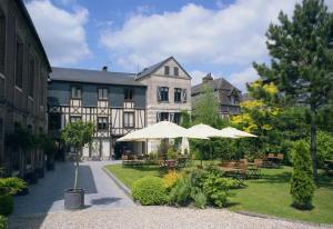 um pátio com mesas e guarda-sóis em frente a um edifício em Hôtel La Licorne & Spa em Lyons-la-Forêt