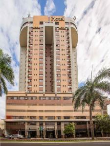 a tall building with palm trees in front of it at Hotel Metrópole Maringá in Maringá