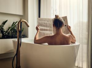 Ein Mann, der in einer Badewanne sitzt und Zeitung liest. in der Unterkunft Contessina Suites & Spa - Adults Only in Planos