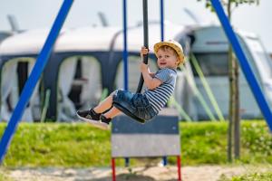 a young boy is sitting on a swing at Camping de Vogel in Hengstdijk