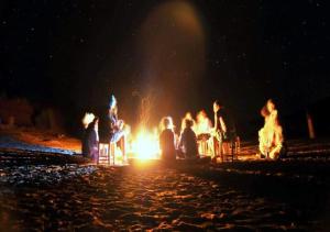 Un gruppo di persone sedute intorno al fuoco di notte di M'hamid Desert Camp Tours a M'Hamid