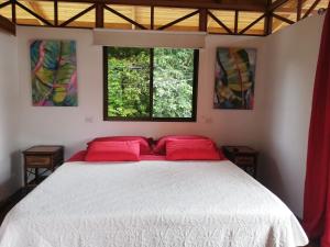 a bedroom with a bed with red pillows and two windows at Ibiza Tropical Beach Villas in Uvita