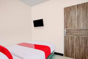 1 dormitorio con 1 cama y TV en la pared en Super OYO Capital O 3198 Sukomanunggal Inn, en Surabaya