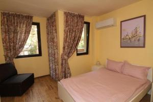 a bedroom with a bed and a chair and two windows at Bendida Apartments in Velingrad
