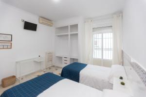 a white bedroom with two beds and a tv at BOHEMIA SANLUCAR in Sanlúcar de Barrameda