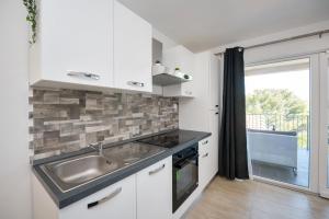 uma cozinha com armários brancos, um lavatório e uma janela em Feel Dugi otok apartments em Luka
