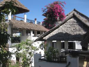 a white building with a thatched roof and a tree with pink flowers at Jannat House in Lamu