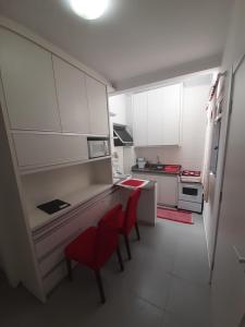una pequeña cocina con armarios blancos y sillas rojas en Apto compacto em Floripa-continente, en Florianópolis