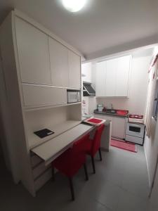 uma pequena cozinha com armários brancos e cadeiras vermelhas em Apto compacto em Floripa-continente em Florianópolis
