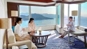 three women sitting in a room with a view of the ocean at Grand Prince Hotel Hiroshima in Hiroshima