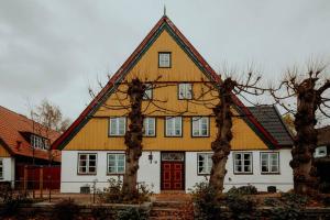 Casa grande de color blanco y amarillo con puerta roja en Altes Fährhaus - Ferienwohnung Unnern, 170 qm, en Wewelsfleth