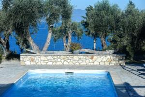a swimming pool with a stone wall and trees at Villa Marmari in Kontogiannátika