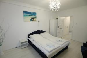 a white bedroom with a bed and a chandelier at Anna apartman in Szeged