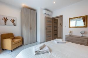 a white bedroom with a bed and a chair at White Sands in Mellieħa