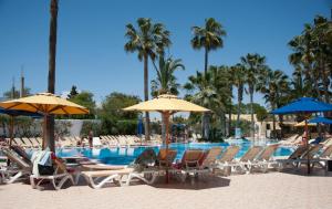 Hotel Nesrine Hammamet في الحمامات: مجموعة كراسي ومظلات بجانب مسبح
