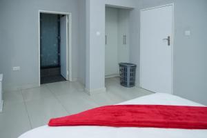 a white bedroom with a red blanket on a bed at Greyville Apartments in Lusaka