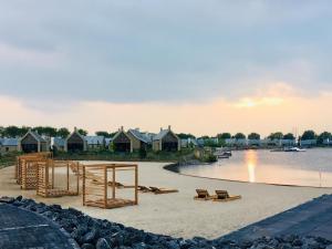 a sandy beach with benches and houses on the water at Holiday Home Oesterdam Resort-1 by Interhome in Tholen