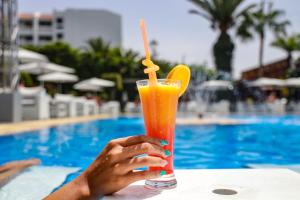 a person holding a glass of orange juice next to a swimming pool at Mabrouk Hotel and Suites- Adult only in Agadir