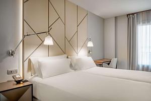 a hotel room with a large white bed and a desk at NH Collection León Plaza Mayor in León