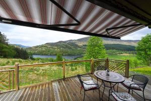 a deck with a table and chairs and a view of a lake at Kingfisher Lodge sleeps up to 4 in Crianlarich