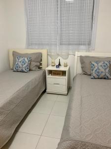 a bedroom with two beds and a nightstand next to a window at Enseada Arvoredos in Guarujá